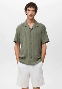 Short-sleeve olive green button-up shirt with vertical stripes, relaxed fit, and a collar, paired with white shorts. Smooth fabric texture.
