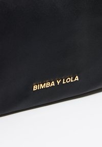 Mustmust kott, millel on tekstureeritud pind ja kuldne relieflogoga "BIMBA Y LOLA" esiküljel. Lihtne disain, ilma täiendavate aksessuaarideta.