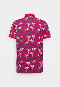 Polo à manches courtes rose vif avec un imprimé de palmiers blancs, bleus et brun foncé, vu de dos sur un fond uni.