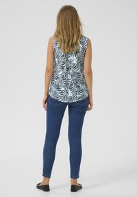 Haut sans manches, bleu clair, avec un motif de feuilles noires, associé à un jean skinny bleu foncé et des ballerines noires. Tissu texturé avec un ourlet arrondi.