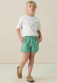 Witte katoenen T-shirt met een klein kleurrijk ontwerp, gecombineerd met lichtgroene textuurshorts met een elastische tailleband en zijzakken.