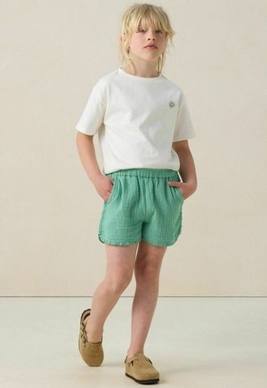 T-shirt en coton blanc avec un petit design coloré, associé à un short texturé vert clair avec une taille élastique et des poches latérales.