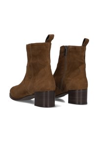 Bruine suede enkellaarsjes met middelhoge blokhak, achterste trekstrookjes en een zijrits aan één laars, gepresenteerd op een witte achtergrond.