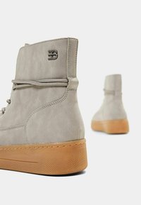 Bottes montantes en daim gris avec une semelle en caoutchouc gomme texturée et un design à lacets. Présentent un accent logo à l'arrière et des détails de coutures.