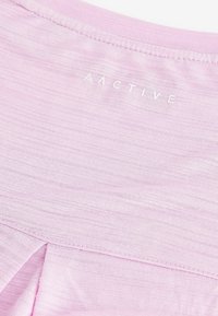 Lys pink aktivtøj top har et blødt, tekstureret stof, med en rund halsudskæring og et logo trykt i hvidt nær sømmen.