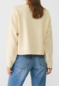 Pull tricoté de couleur crème avec une coupe décontractée, ourlet côtelé et épaules tombantes, associé à un jean taille haute bleu clair.