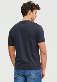 Granatowa koszulka z krótkim rękawem wykonana z miękkiej bawełny, z okrągłym dekoltem i gładką fakturą. Noszona z jasnoniebieskimi dżinsami.