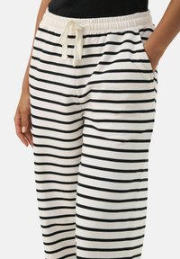 Pantalons de jogging rayés en tissu doux, avec des rayures horizontales noires et blanches, taille élastique avec cordon de serrage et poches latérales.