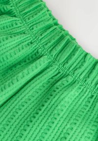 Tela de algodón verde con un patrón texturizado, que presenta diseños acanalados verticales y horizontales y una cintura elástica.