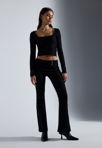 Schwarzes, langärmliges Cropped-Top mit strukturiertem Muster, kombiniert mit hoch taillierten schwarzen Hosen mit Knopfverschluss und schmaler Passform.