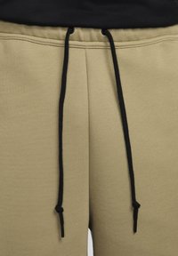 Ljus olivgrön sweatshirtbyxor med mjuk textur, med svarta dragsnören och elastisk midja. Inga synliga logotyper eller mönster.