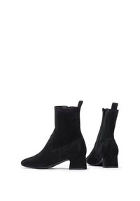 Stivaletti in suede neri con tacco basso a blocco, cerniera laterale e linguette di sollevamento, mostrati da angolazioni laterali e posteriori su sfondo bianco.