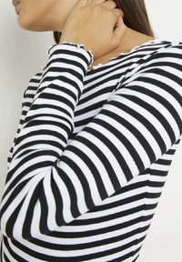 Svart och vit randig långärmad tröja med ribbad textur. Har en scallop-krage och fransiga ärmupphor, vilket framhäver den avslappnade designen.