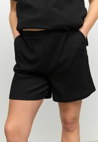 Pantaloni corti neri con tessuto texturizzato, vita elasticizzata e tasche laterali. Il design è semplice, con un taglio dritto e senza modelli visibili.