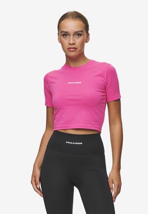 Rosa cropped t-skjorte med korte ermer, har hvit "PEGADOR" logo på forsiden. Kombinert med høytlivs svarte leggings.