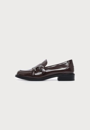 Mocassin en cuir marron foncé avec double boucle argentée et petit talon noir empilé, vu de profil sur un fond clair uni.