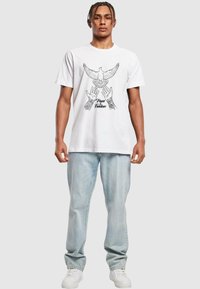 White cotton t-shirt featuring a black graphic of a dove above open hands with "Peace & Freedom" text below. Paired with light blue jeans.