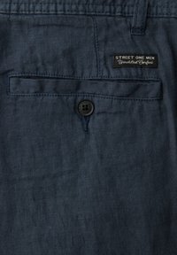 Ciemnoniebieska tkanina z zapinanym na guziki tylnym kieszonką i małą prostokątną czarną metką z napisem "STREET ONE MEN Unmatched Comfort."