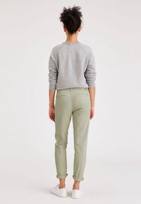 Grå sweatshirt med ribbade ärmar, olivgröna tapered byxor med uppvikt fåll och vita sneakers, sedd bakifrån.