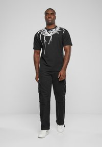 Sort bomulds t-shirt med hvid grafikdesign ved halsen, parret med sorte cargo-bukser med flere lommer og hvide sneakers.