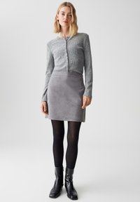 Cardigan grigio lavorato a maglia con bottoni, abbinato a una mini gonna in suede grigia. Calze nere e stivaletti completano l'outfit. Design semplice e moderno.