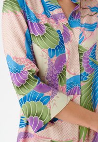 Blusa di satin con un motivo di piume colorate nei toni del verde, viola e blu, dotata di colletto e maniche arrotolate. Tessuto liscio.