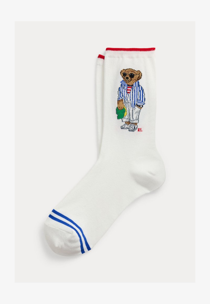 Λευκή κάλτσα με κόκκινη μανσέτα και μπλε ρίγες στο δάχτυλο, με απεικόνιση αρκούδας που φοράει γυαλιά ηλίου, ριγέ μπουφάν, άσπρο παντελόνι και κρατάει πράσινο καπέλο.