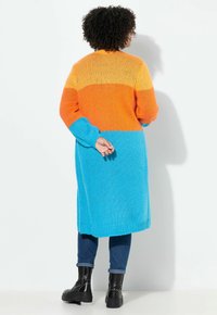 Cardigan a maglia di lunghezza al ginocchio in arancione, giallo e blu. Presenta maniche lunghe e vestibilità morbida con polsini e orlo a coste.