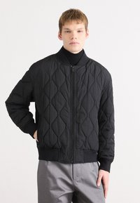 Μαύρο καπιτονέ μπουφάν bomber με όρθιο γιακά, κλείσιμο μπροστά με φερμουάρ, ριμπ μανσέτες και ίσιο τελείωμα, διαθέτοντας υφασμάτινο διαμαντέ σχέδιο.