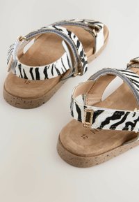 Sandali con motivo zebra, con soletta in fascia tan imbottita, cinturini grigi e hardware in tono oro. La suola presenta un design maculato.