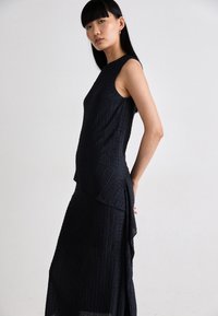 Sleeveless black dress with a textured design and asymmetrical hem, featuring a flared lower section and a smooth, elegant silhouette.