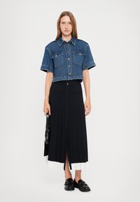 Jeans skjorte med korte ermer og knappestolpe, kombinert med en svart maksimal skjørt med frynser og hvit kant, samt svarte loafers med detaljer.