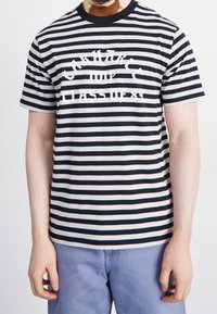Černobílý pruhovaný tričko s krátkými rukávy, na hrudi s velkým bílým grafickým textem "CARHARTT WIP CLASS OF 89".