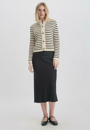 Gestreepte cardigan in crème en zwart, met een knoopsluiting aan de voorkant, geribbelde manchetten, gecombineerd met een strakke zwarte midirok en platte schoenen.