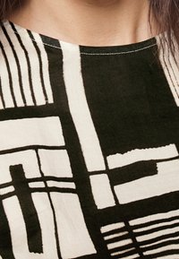 Prenda de color negro y crema con un patrón que presenta líneas y formas geométricas, con un escote redondo y tejido texturizado.