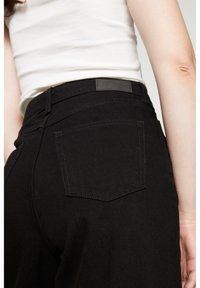 Schwarze Jeans mit hoher Taille, ausgestattet mit zwei Gesäßtaschen, farblich abgestimmter Naht und einem minimalistischen Leder-Logopatch am Bund.