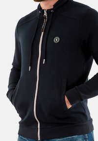 Marine blauwe zip-up hoodie gemaakt van een gladde stof, met een hoge kraag, trekkoord, zijzakken en een rond logo op de borst.