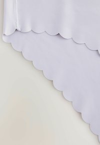 Tessuto viola chiaro con una texture liscia, caratterizzato da un design a bordi ondulati lungo il fondo. Finitura morbida e stile minimalista.