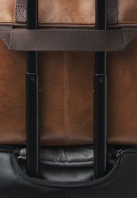 Braune Ledergepäckstücke mit schwarzem Boden, ausgestattet mit einem ausziehbaren Griff, einem Reißverschlussfach und einem gesteppte grauen Innenauskleidung.