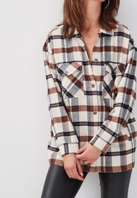 Plaid flannel shirt in beige, brown, and blue. Features two chest pockets, button closure, and a relaxed fit, with long sleeves.