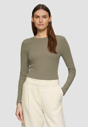 Olijfgroene ribbeltrui met lange mouwen en een ronde hals; gedragen met crèmekleurige hoge taillebroek. Eenvoudig, aansluitend ontwerp.
