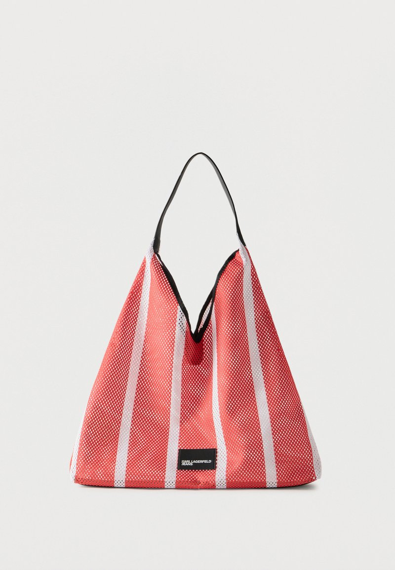 Τσάντα ώμου με κόκκινες και λευκές ρίγες, μαύρο περίγραμμα και ένα μαύρο λουρί ώμου, με μια μικρή μαύρη ετικέτα στο κάτω κέντρο.