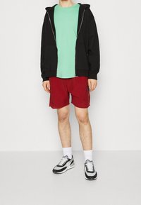 Černá mikina na zip, mentolové tričko, červené šortky, bílé ponožky a černobílé tenisky. Neformální outfit s kontrastními barvami.