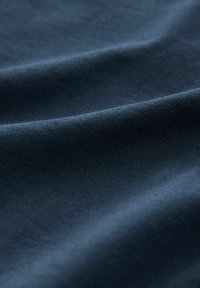 Dark blue fabric with soft, smooth texture and gentle folds creating subtle shadows and highlights across the surface.