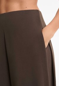 Braune, hoch taillierte Hose aus glattem Stoff mit einer Seitentasche und dezenten Nähdetails. Lockerer, weit geschnittener Stil.