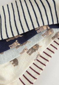 Vier gevouwen gebreide kledingstukken met verschillende patronen: marineblauwe en witte strepen, dierenmotieven op marineblauw en lichtgrijs, beige met dierenmotieven, en wit met bordeauxrode strepen.