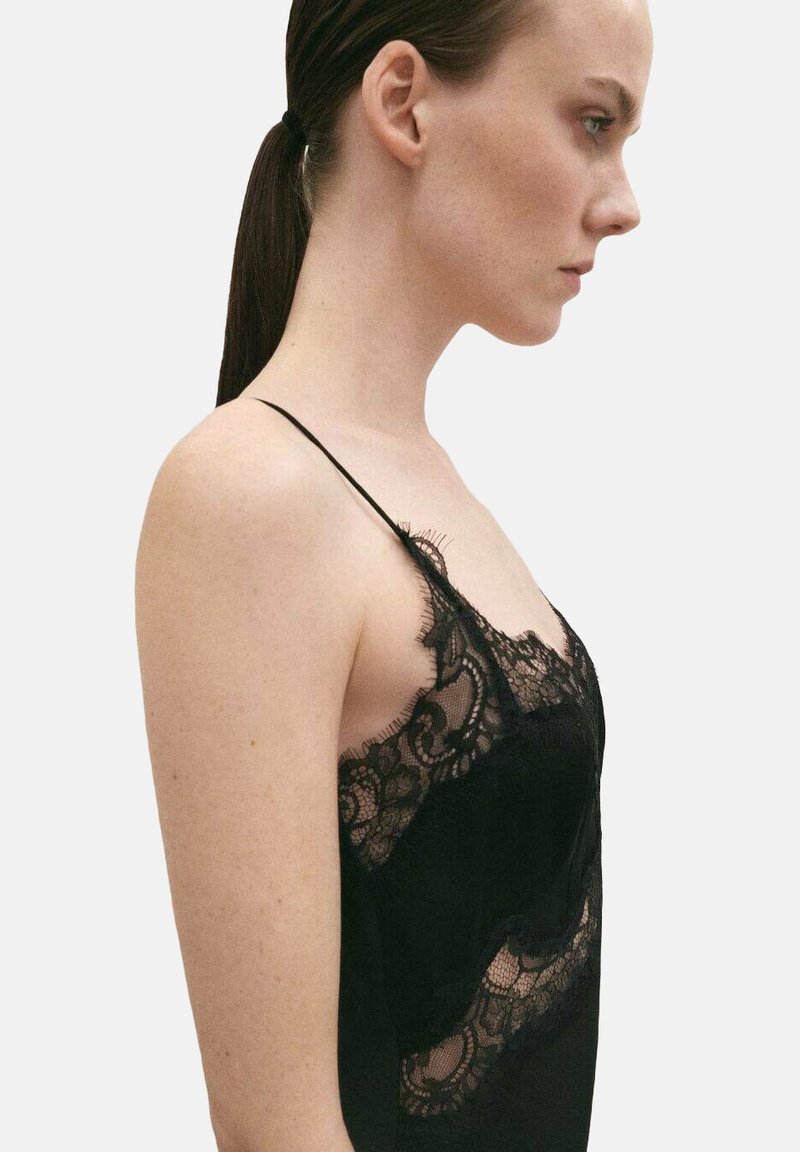 Camisola negra con detalles de encaje, presenta tirantes finos y un delicado borde de encaje a lo largo de los bordes, mostrando una textura transparente.