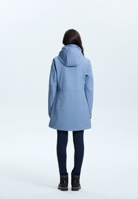 Blaue wasserdichte Jacke mit Kapuze, strukturiertem Design, tailliert und mittellang. Kombiniert mit marineblauen Leggings und schwarzen Stiefeletten.
