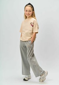 Tricou bej cu mânecă scurtă cu grafică de cireșe; pantaloni gri cu croială largă și accente brodate. Purtați cu adidași albi și gri.