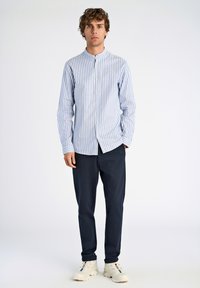 Koszula zapinana na guziki w niebiesko-białe paski, z kołnierzykiem typu band. Połączona z ciemnoniebieskimi spodniami i białymi butami sportowymi. Gładka tekstura materiału.